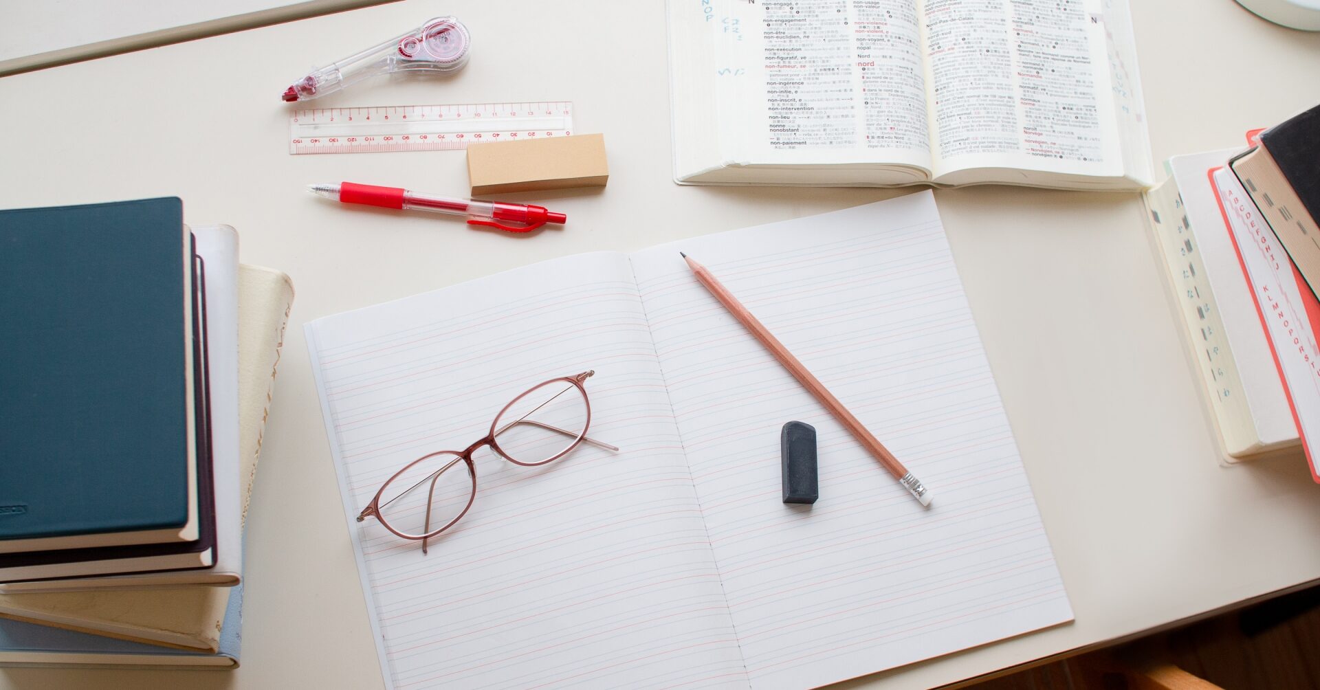 机の上に開いたノートや参考書、メガネなどの勉強道具が並び、受験勉強に集中するイメージ