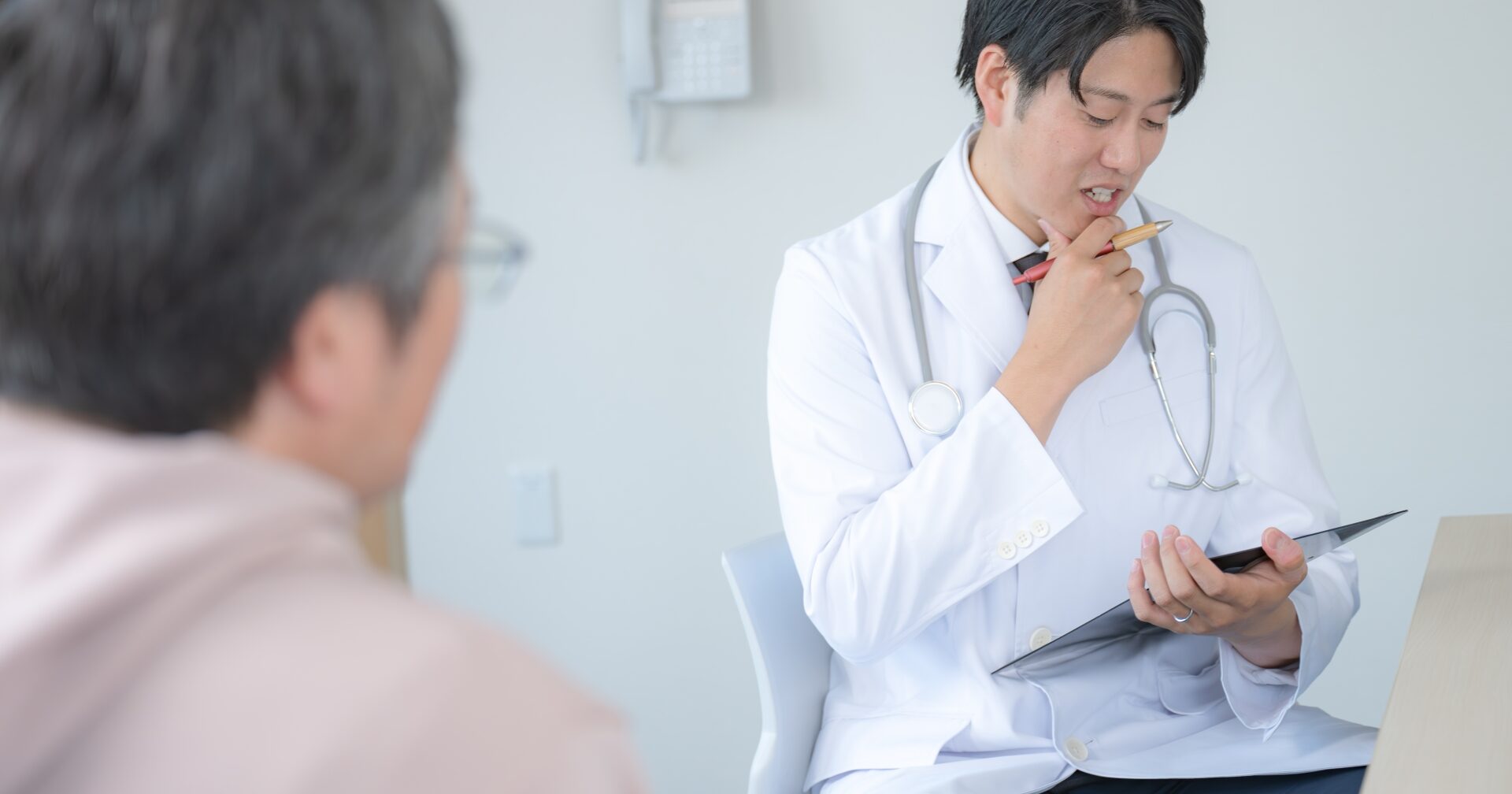 カウンセリングルームで問診票を手に患者と向き合い、説明を行う若い男性医師
