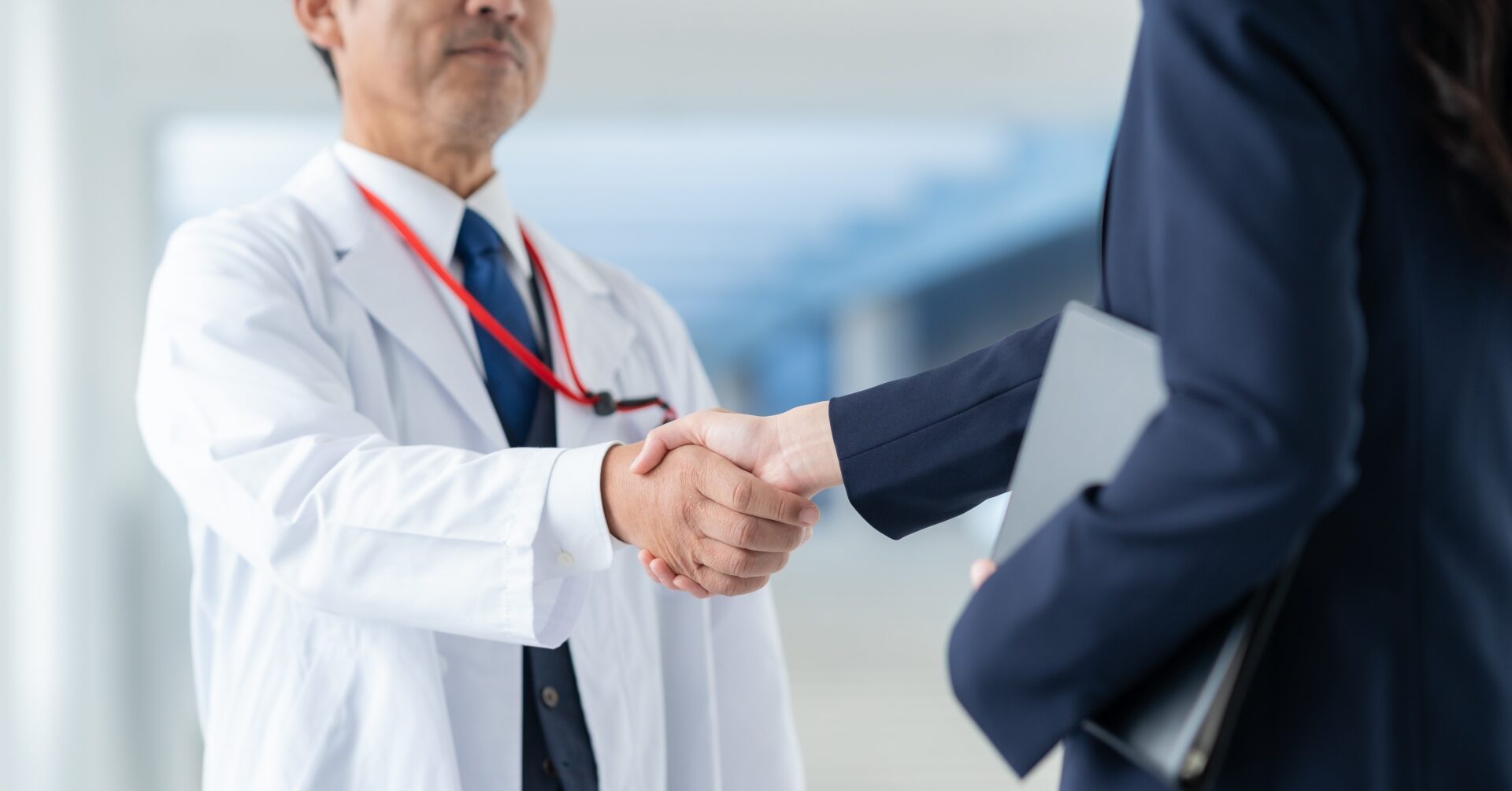 病院経営でのコスト戦略を担う医療経営士の活用イメージ：白衣の医師とスーツ姿の経営担当者が握手する様子。