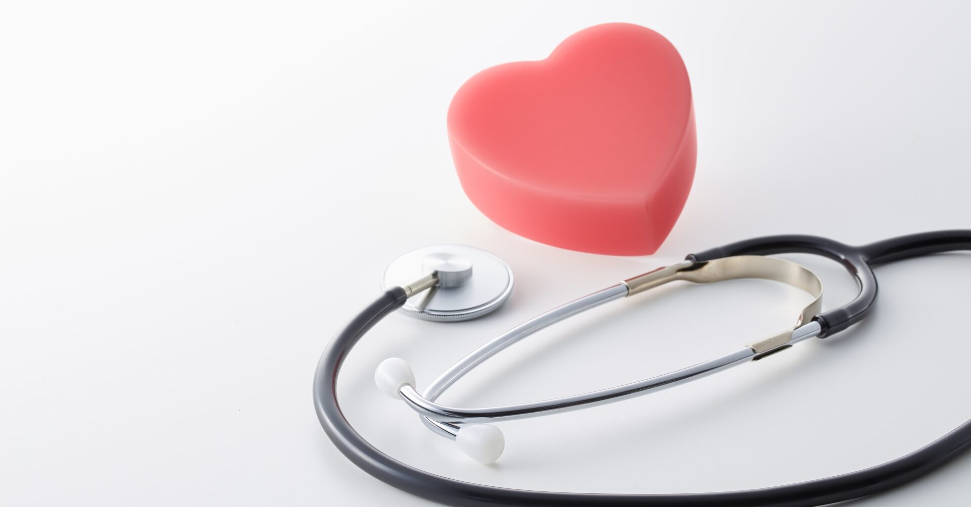 白いデスクの上に黒いチューブの聴診器と赤いハート型オブジェが並べられている