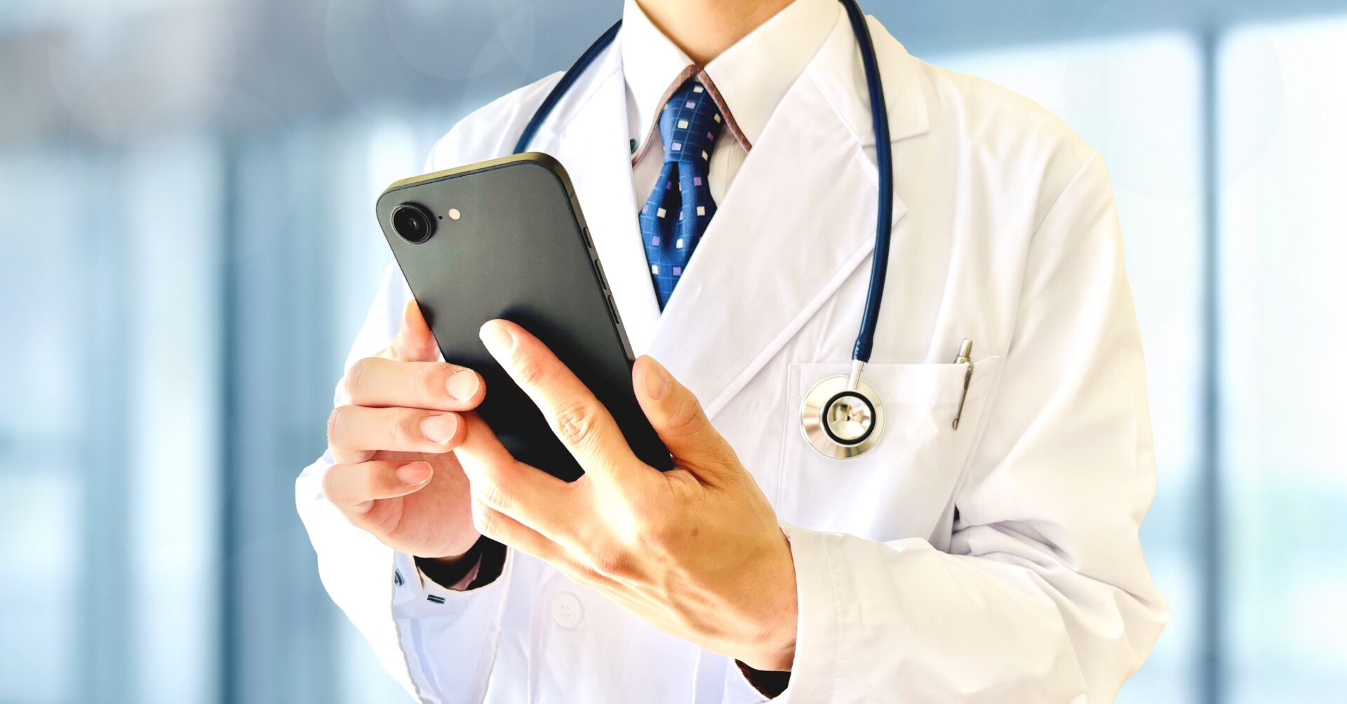 白衣に聴診器をかけた医師が、スマートフォンを操作している様子。医師の情報発信、SNSやメディア活用を象徴するアイキャッチ。