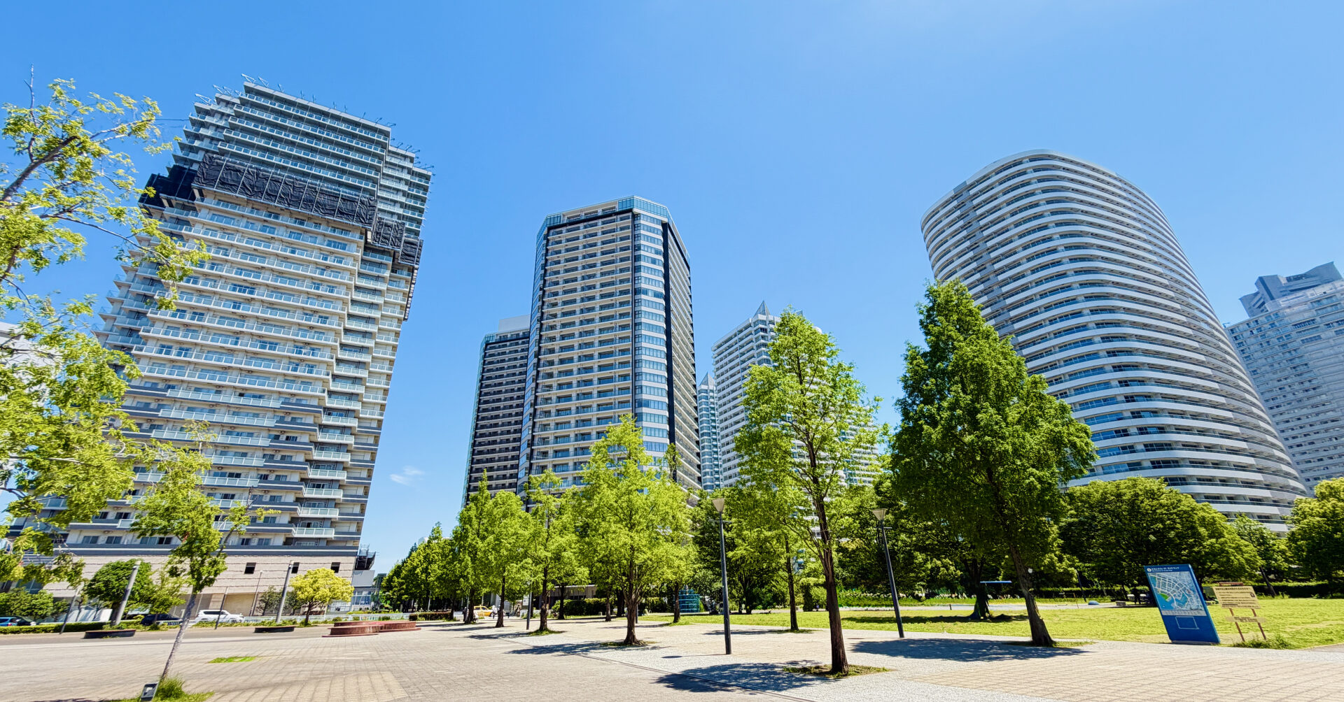 青空の下に並ぶ高層マンションと緑豊かな街並み。医師の賃貸探しイメージを表す都市の住宅エリアの風景